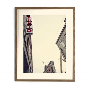 Photographie encadrée d'une enseigne verticale rouge « PHOTO » sur un bâtiment ancien, vue en contre-plongée urbaine